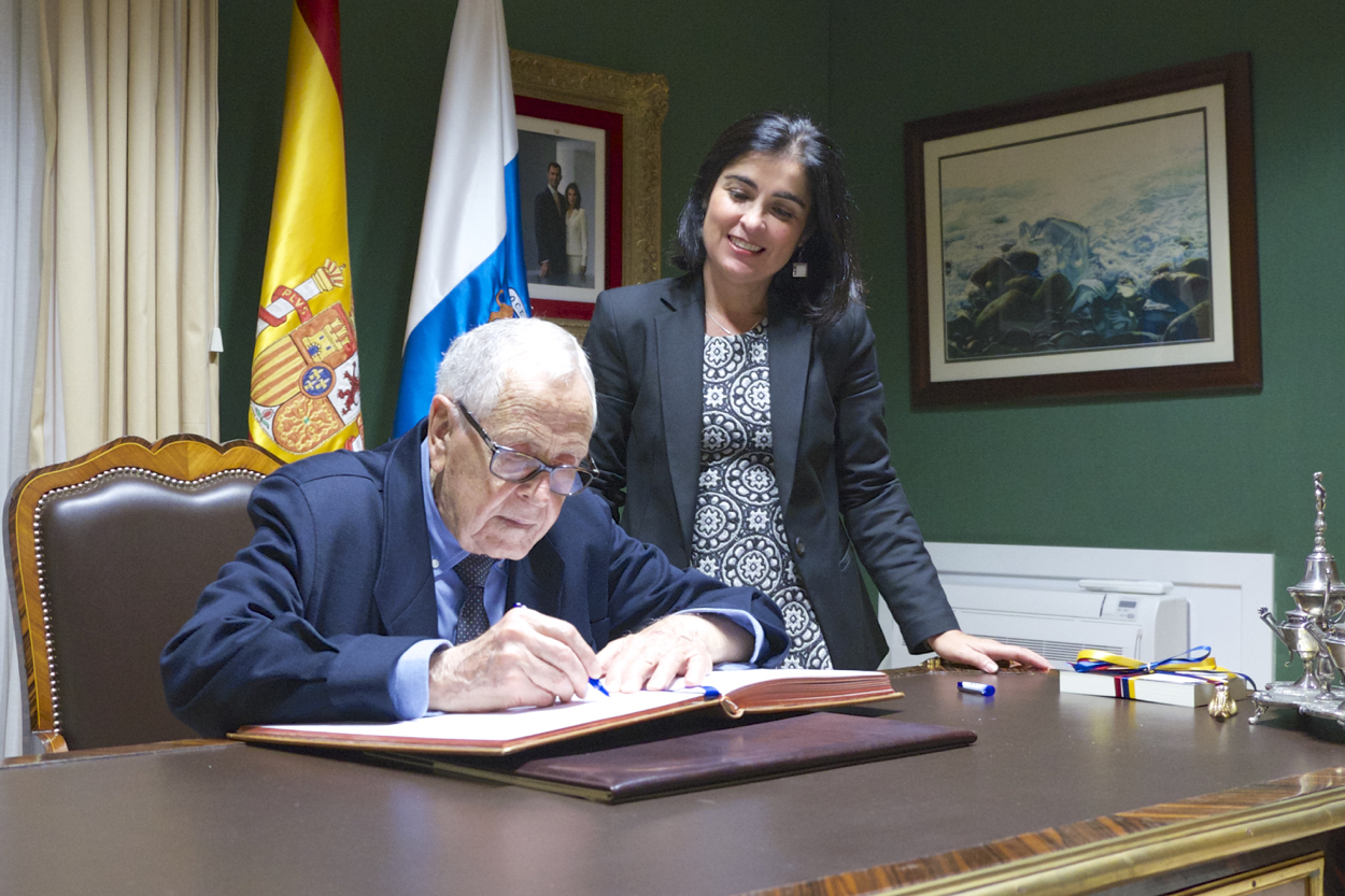 Martín Chirino firma en el libro de honor del Parlamento acompañado por Carolina Darias.