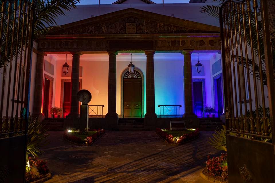 Foto de la fachada del Parlamento de Canarias iluminada con los colores del arcoíris